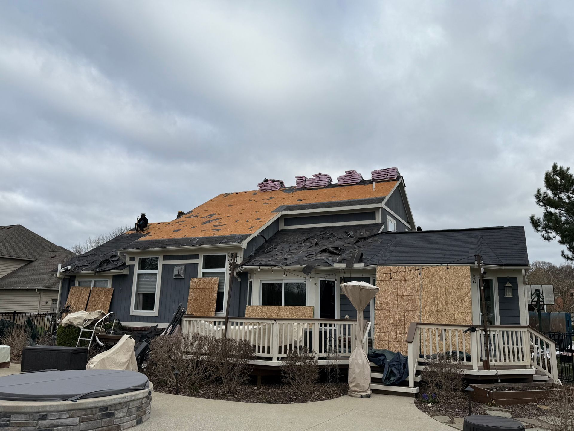House under roof repair; blue siding, deck, partially exposed plywood. Cloudy sky overhead.