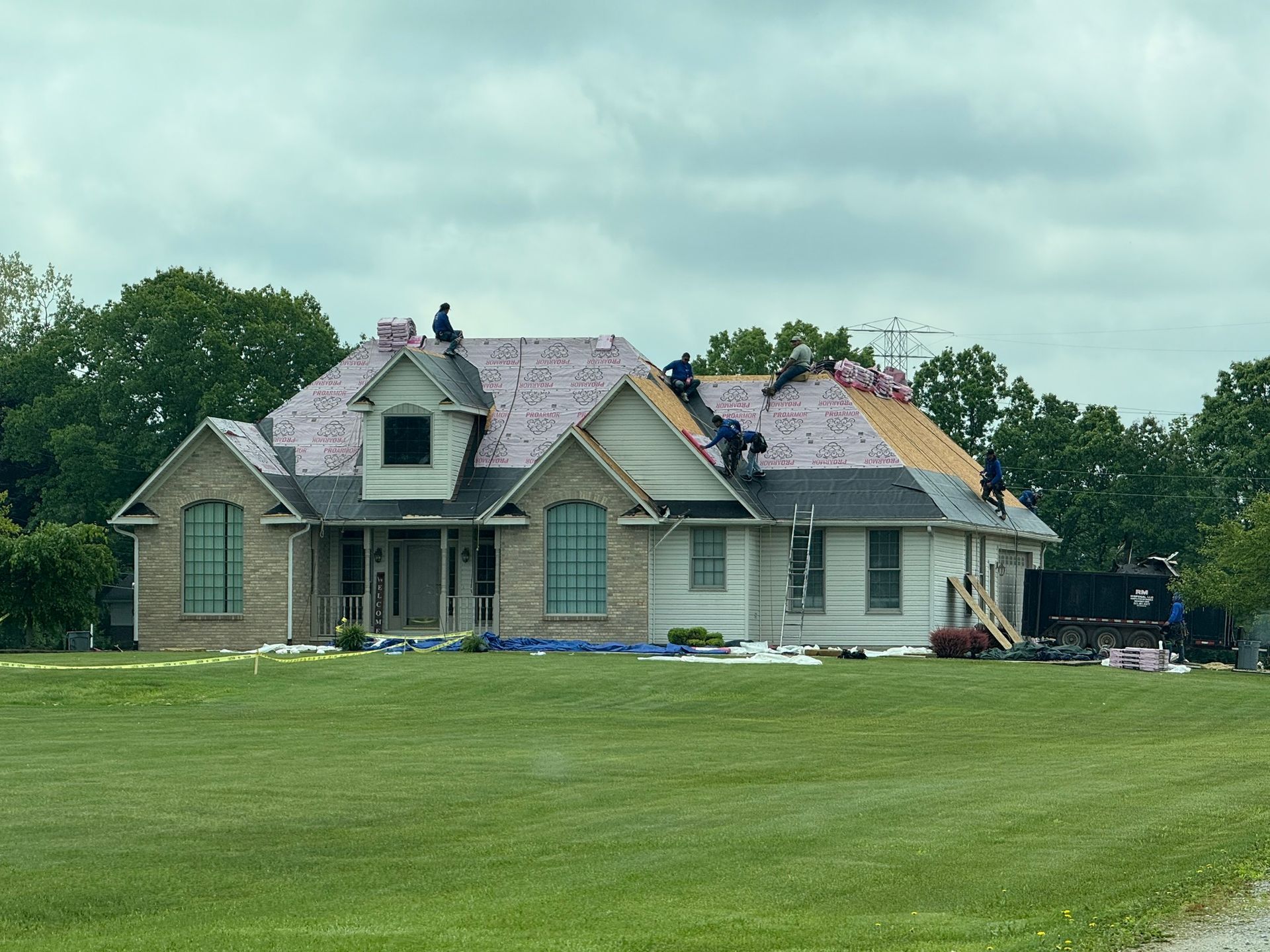 Roofers working on a house with a brick and light-colored exterior on a cloudy day.