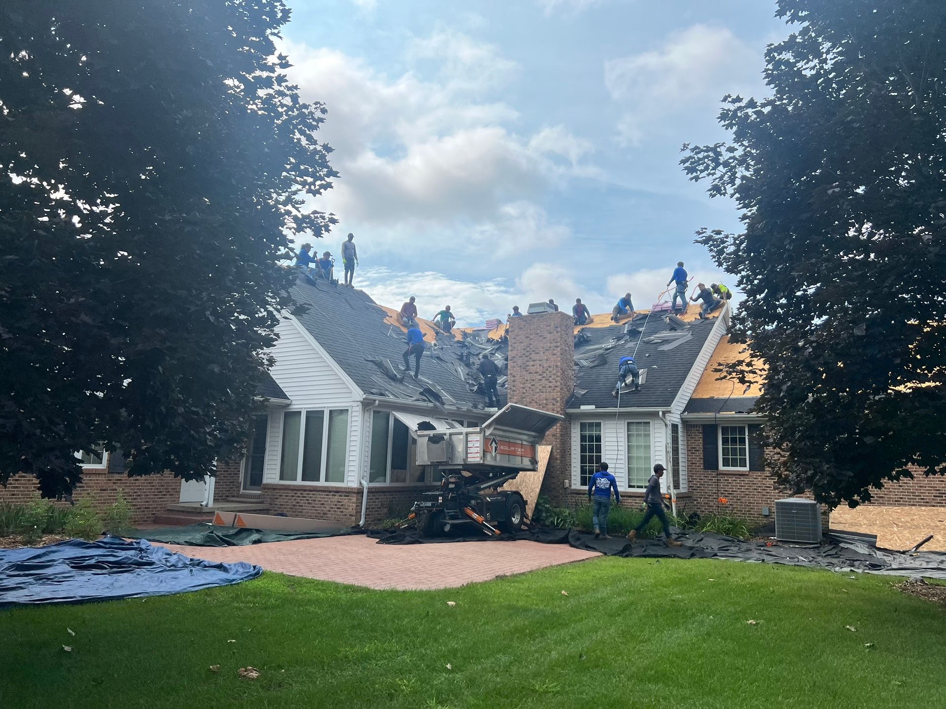 Roofers working on a house with many people on the roof under a cloudy sky.