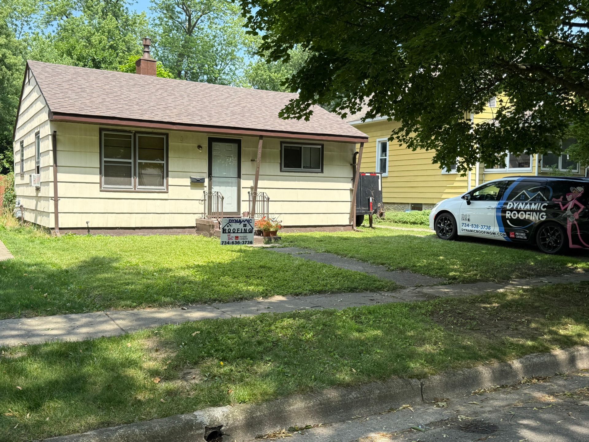 Tan house with overgrown lawn; car with logo parked nearby.