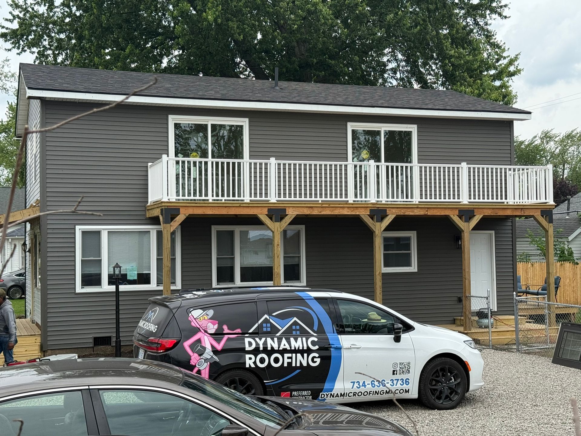 Two-story house with gray siding and a balcony. Dynamic Roofing van is parked in front.