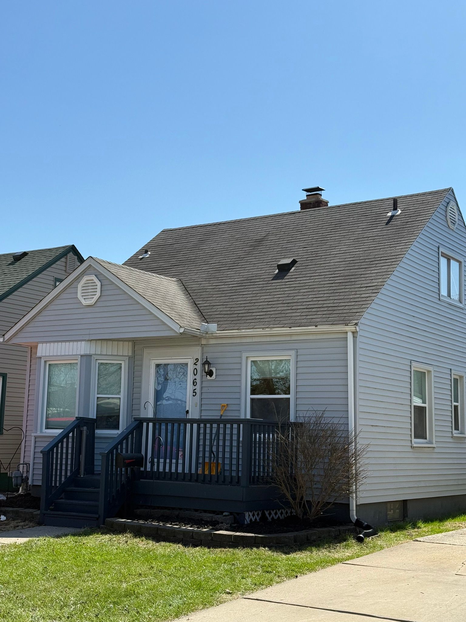 A small blue house with a porch and dark roof on a sunny day.
