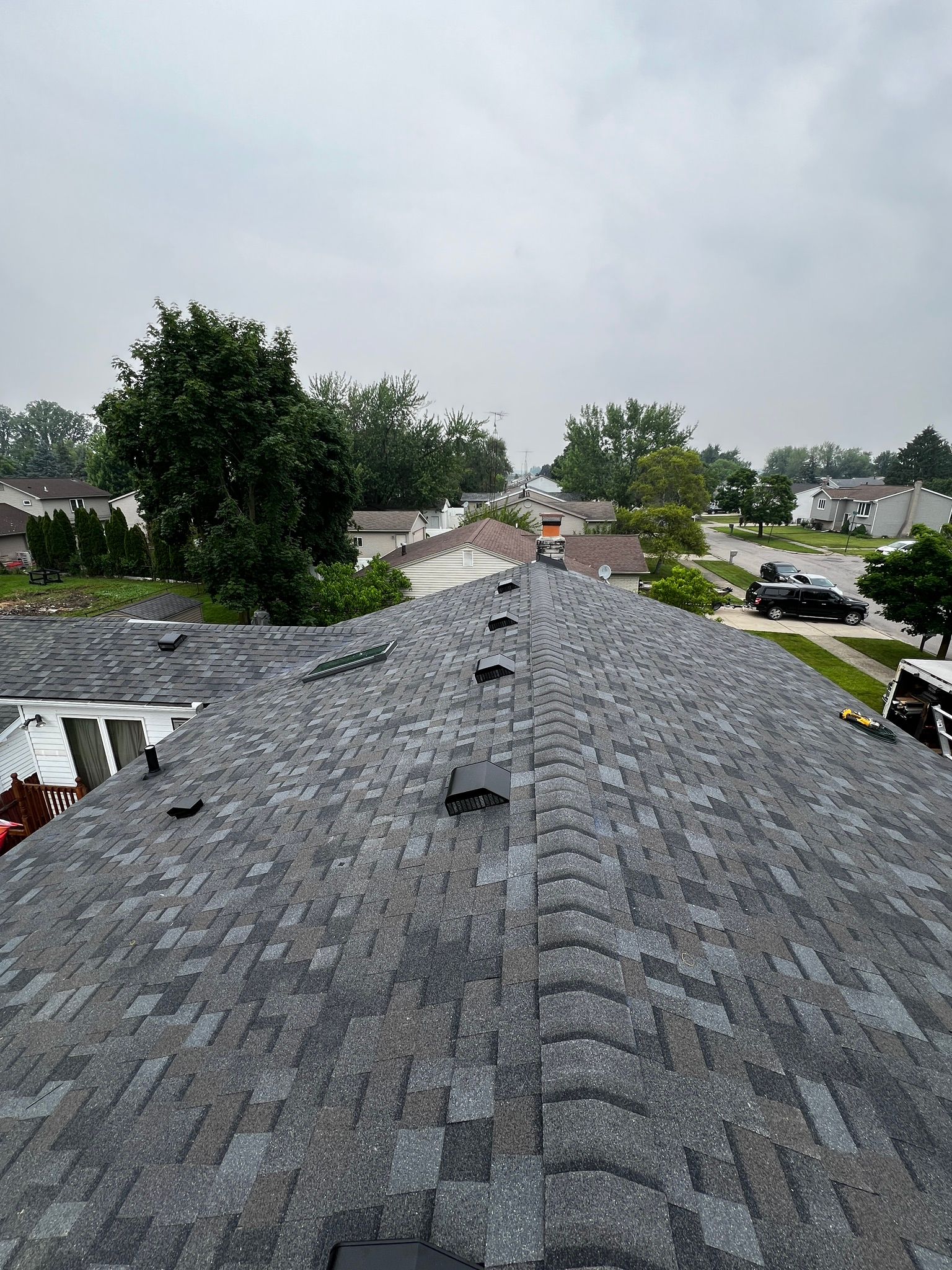 Newly shingled asphalt roof, gray and black, looking over a suburban neighborhood on a cloudy day.