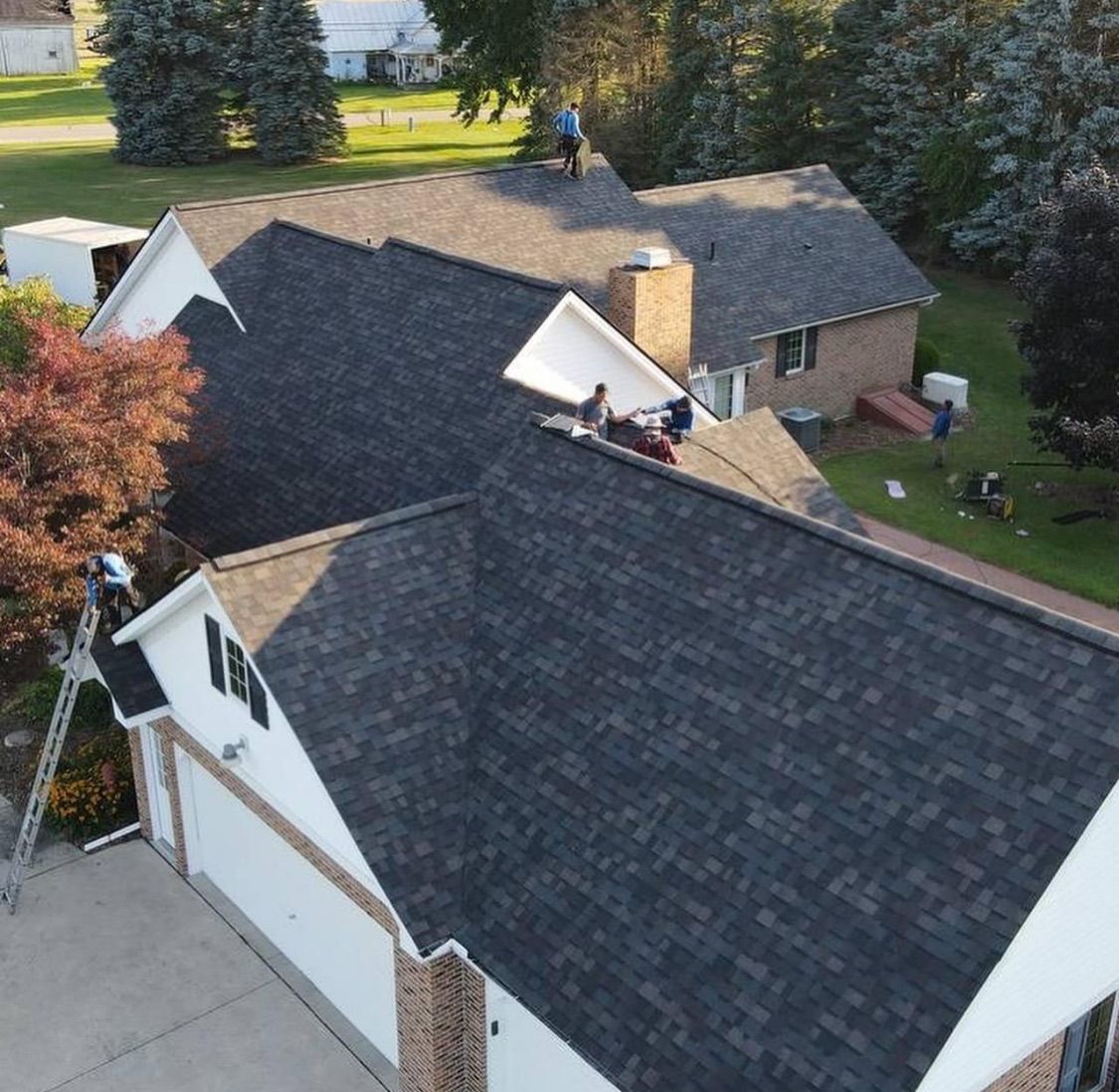 Roofers working on a house with gray shingles; the sky is clear and bright.