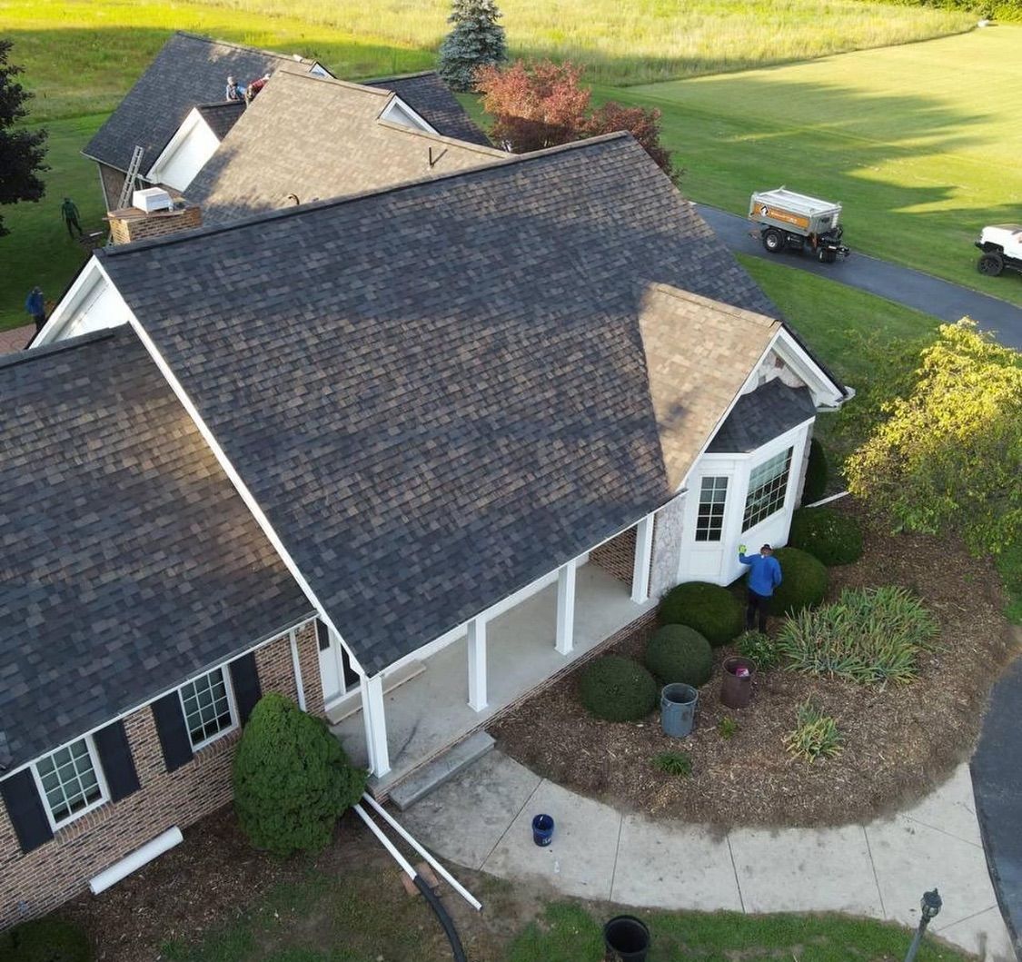 A house with dark gray roof, brick siding, and white trim; a person works near the front porch.