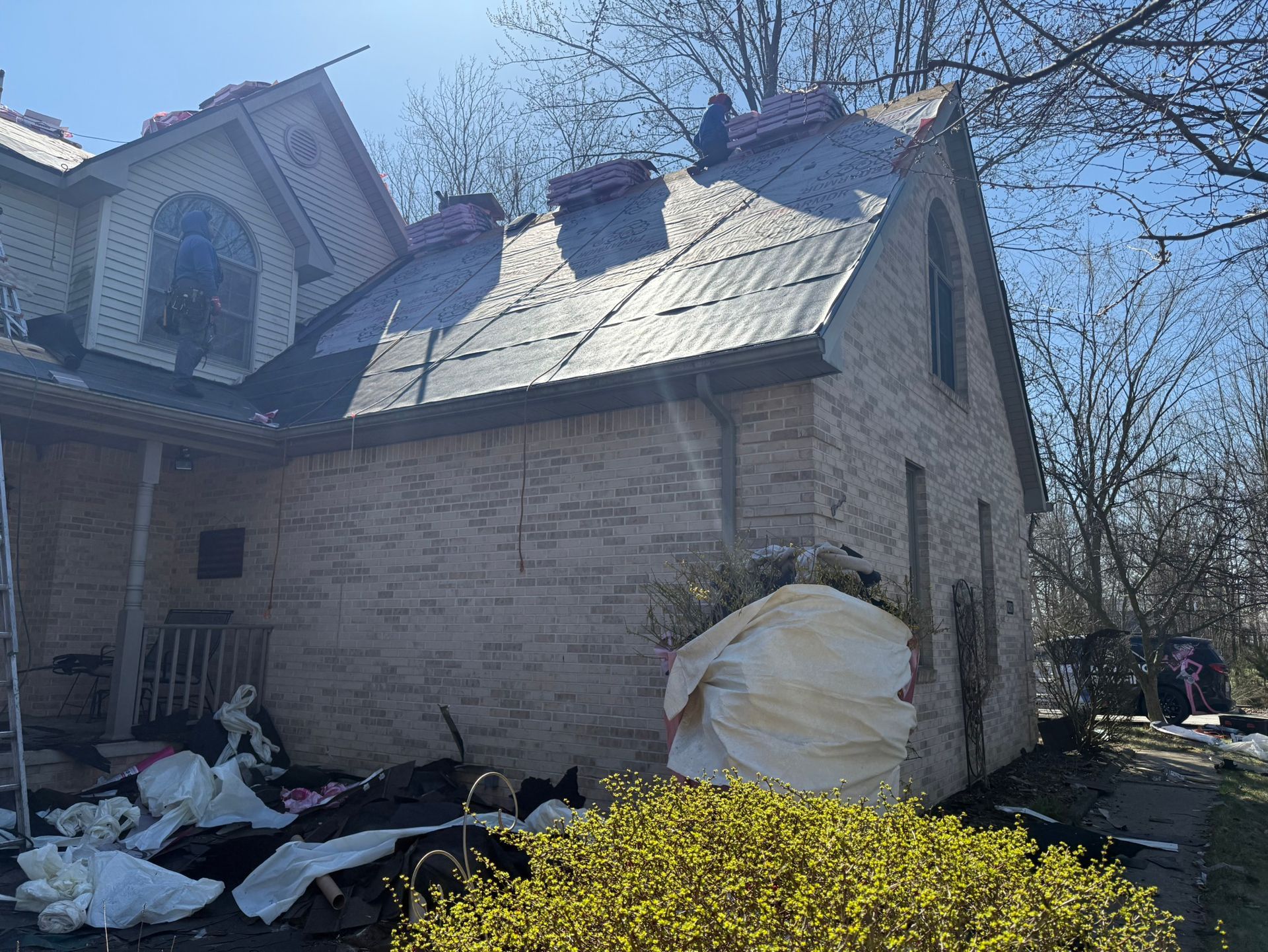 House with partially removed roof, brick facade, debris on ground, sunny day.