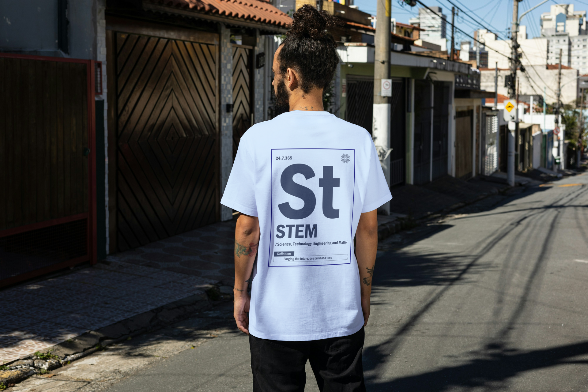 A man wearing a white t-shirt with the word stem on the back is standing on a street.