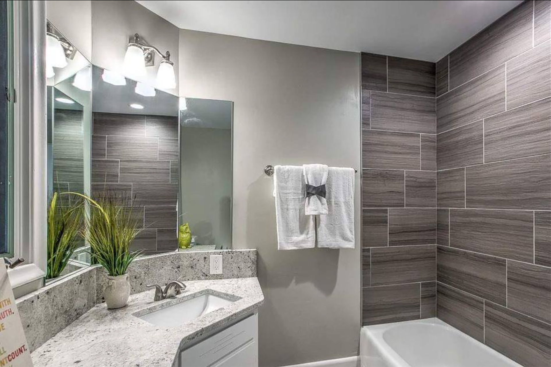 Modern bathroom with gray tiled walls, granite countertop, and white towels.