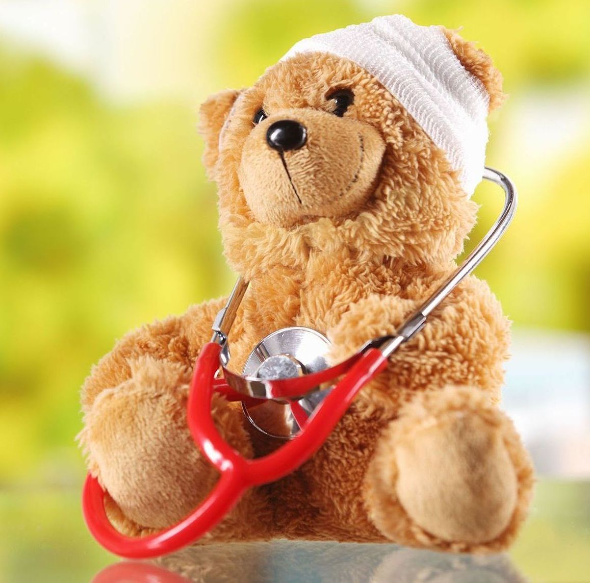 A teddy bear with a bandage on its head is holding a stethoscope.