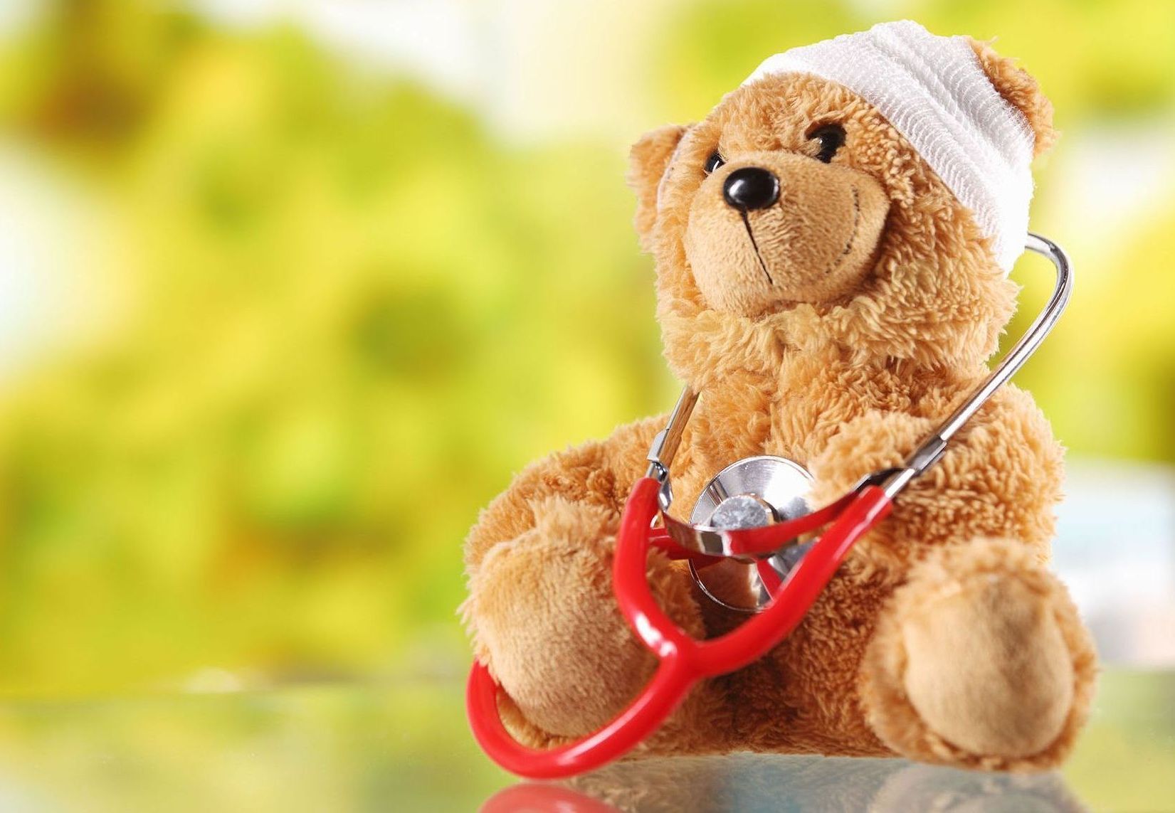 A teddy bear with a bandage on its head is holding a stethoscope.