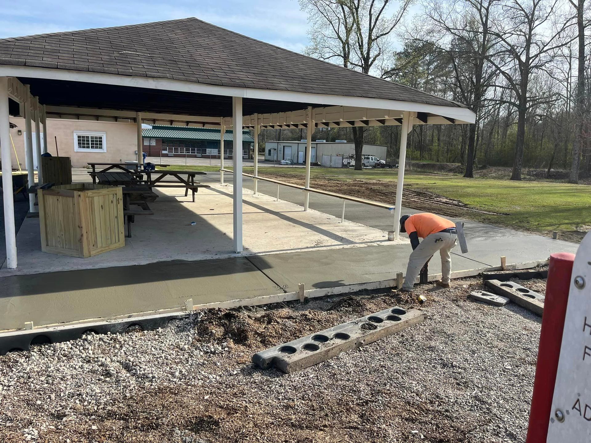 A man is working on a sidewalk in front of a pavilion.