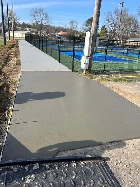A concrete walkway is being built next to a tennis court.