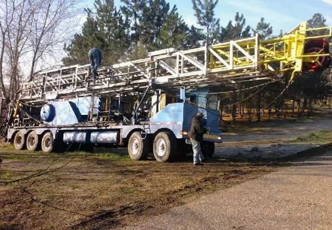 Truck carrying a large white drilling rig being set up outdoors with two people nearby