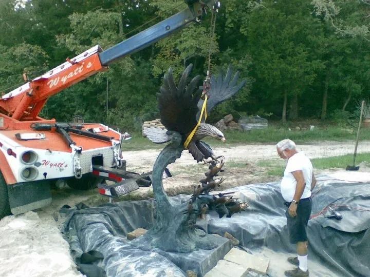 Tow truck lifting a tangled black car body while a man stands beside it at a gravel site
