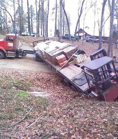 Overturned truck carrying debris on a grassy roadside in a wooded area