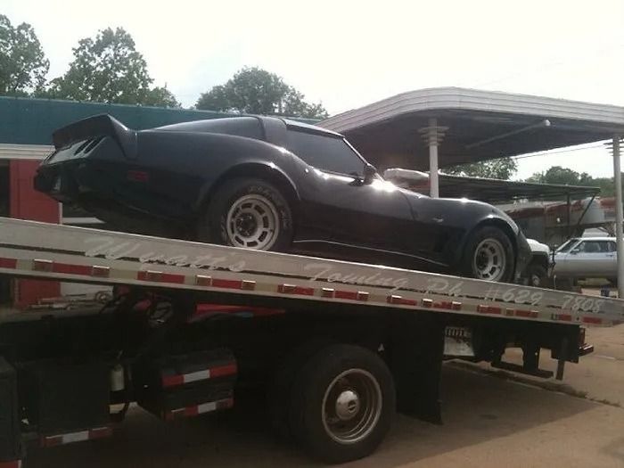 Black sports car strapped on a tow truck flatbed under a carport