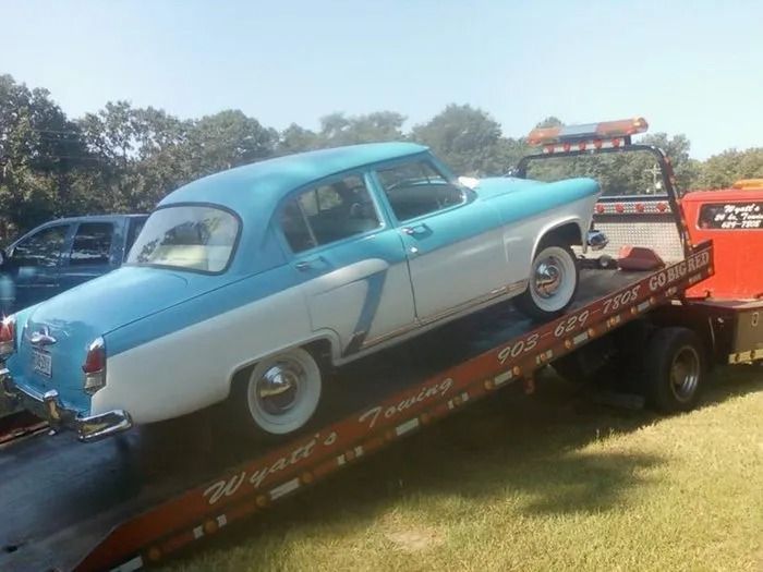 Blue-and-white vintage car being loaded onto a tow truck ramp outdoors