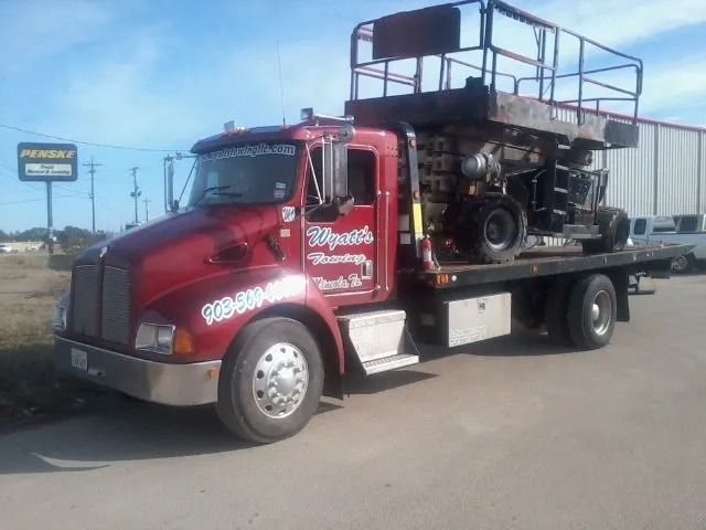 Red semi truck carrying a race car on a flatbed, parked on a roadside.