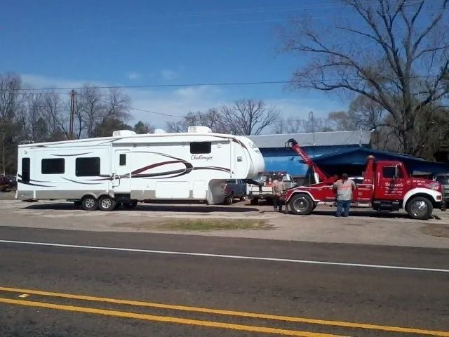 White RV on roadside being towed by red tow truck under clear blue sky