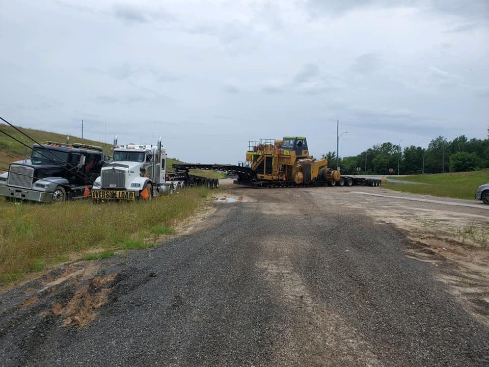Roadside construction site with heavy equipment and trucks on a gravel surface under cloudy skies