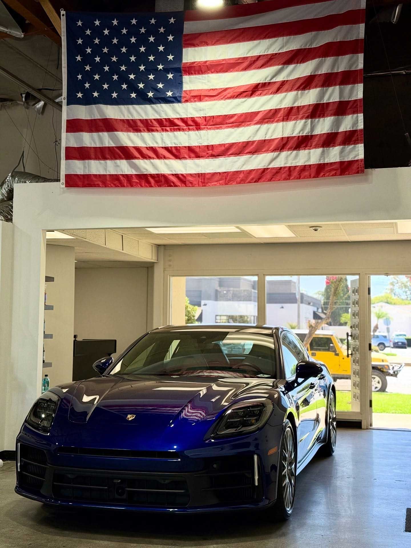 A blue car parked inside a garage, with an American flag hanging above it.
