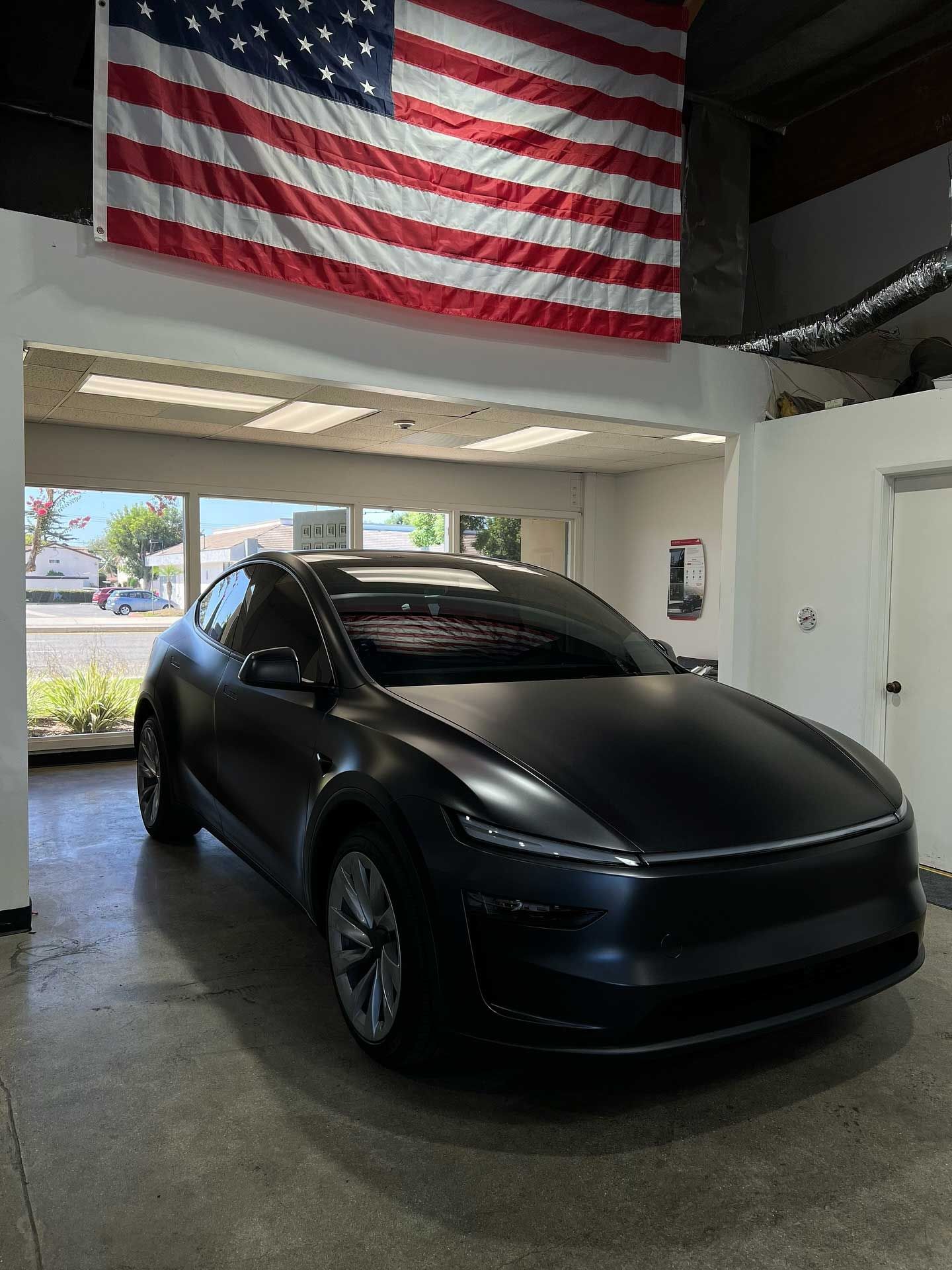 Black electric car parked inside a garage with an American flag hanging above it.