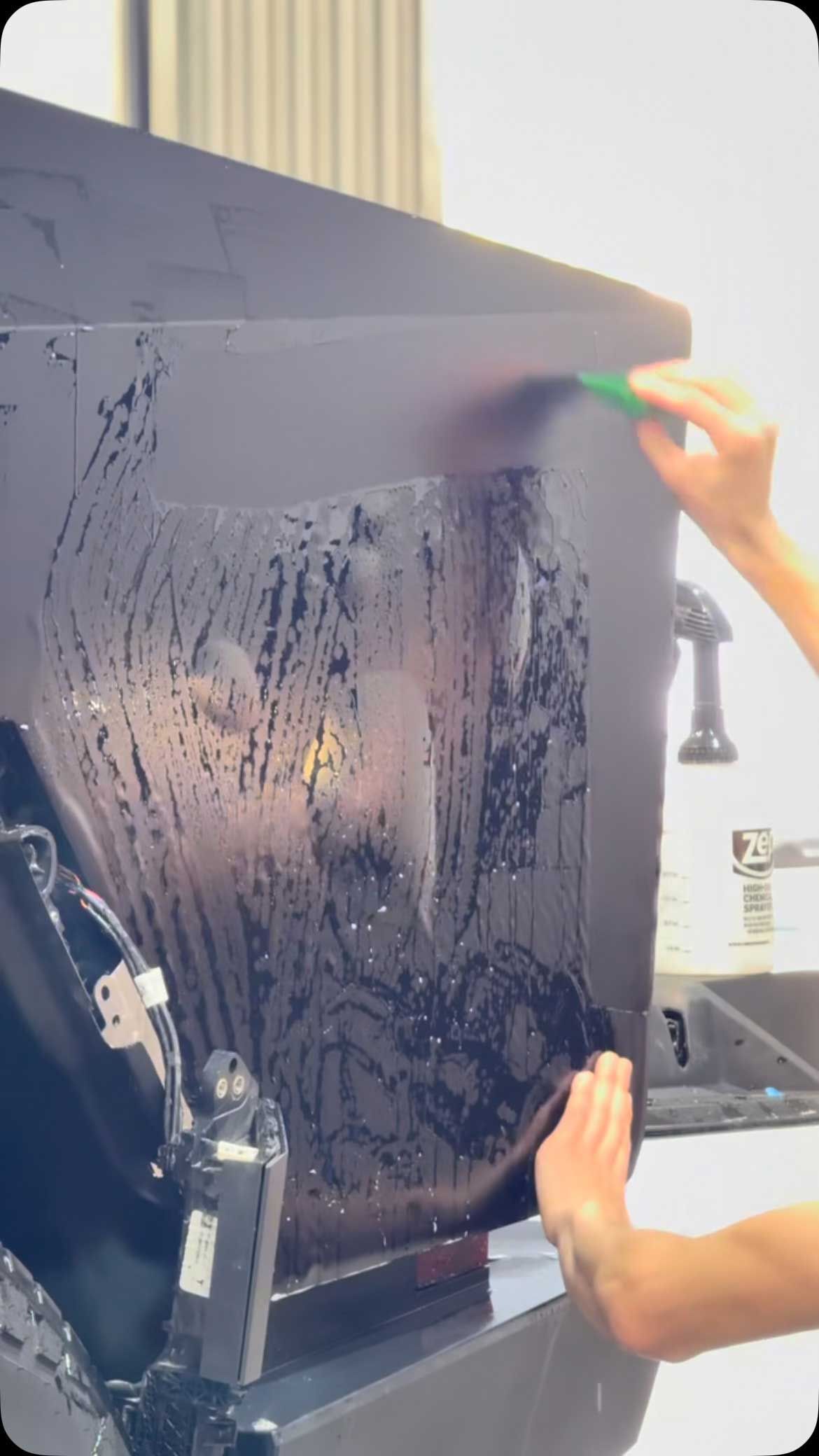 A person applies tinted film to a window, smoothing it with a squeegee.