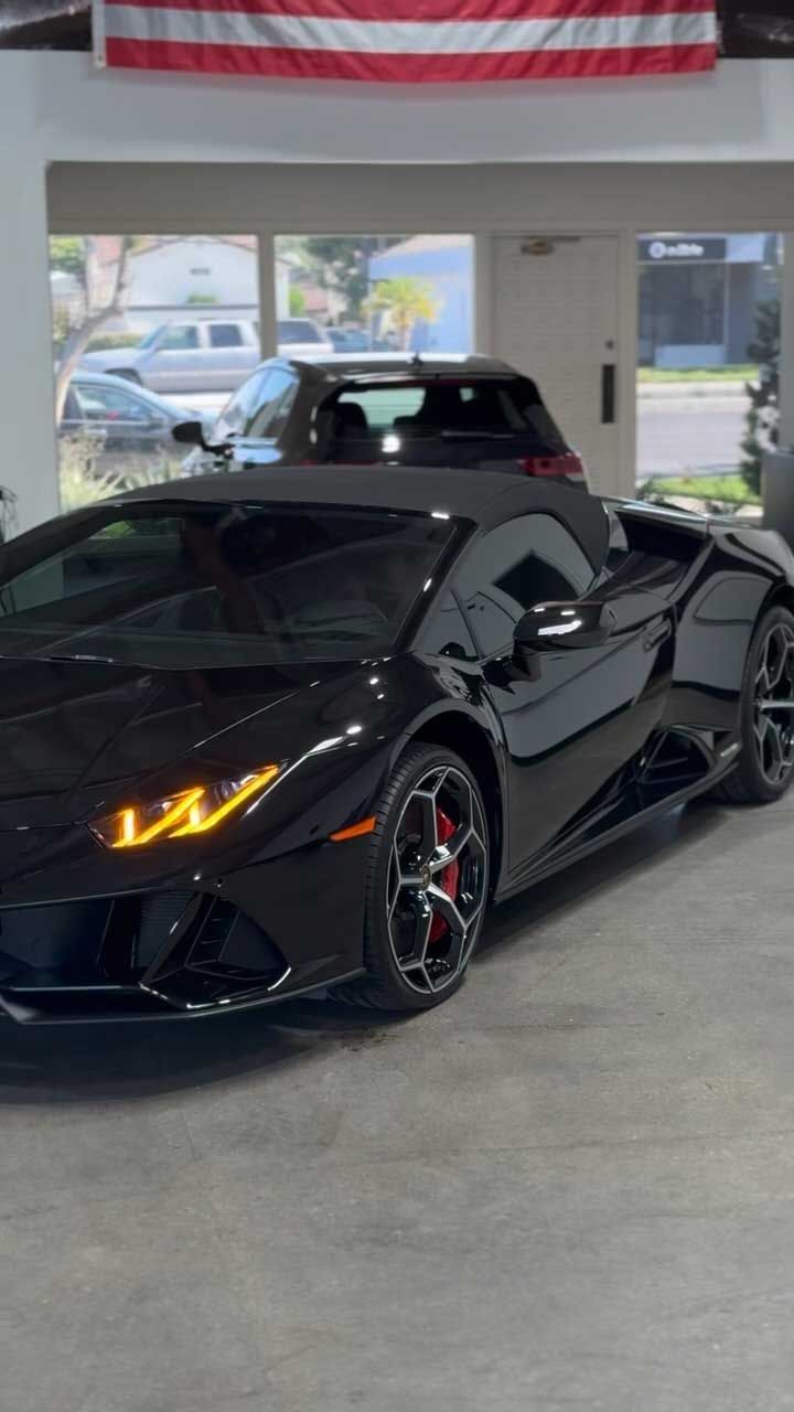 Black Lamborghini Huracan Spyder convertible parked inside a showroom. Red brake calipers visible.