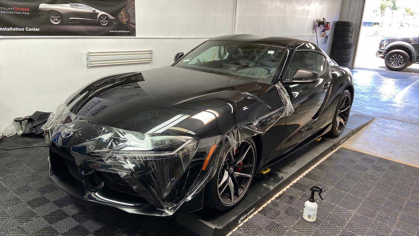 Black sports car with protective film applied, in a garage setting.