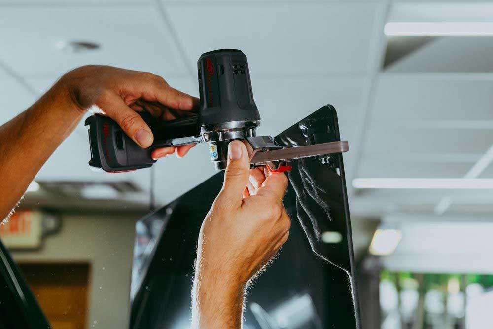 Person using a heat gun to apply film to a car window in a workshop.