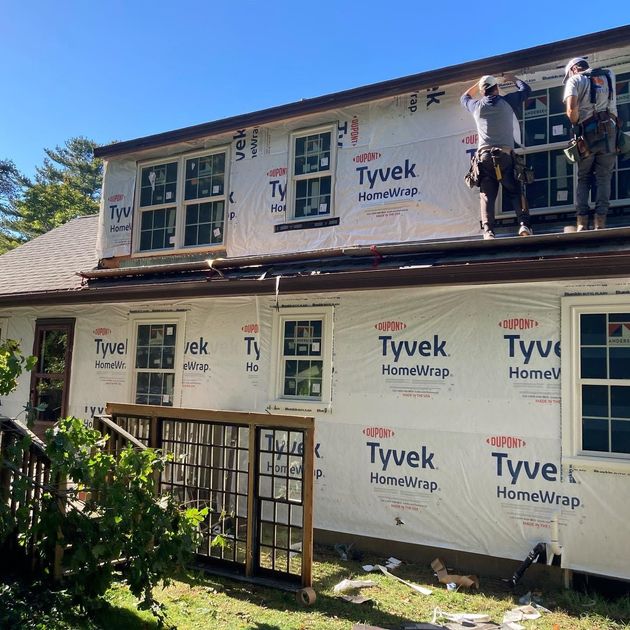 Workers installing Tyvek HomeWrap on a house exterior roof and upper walls