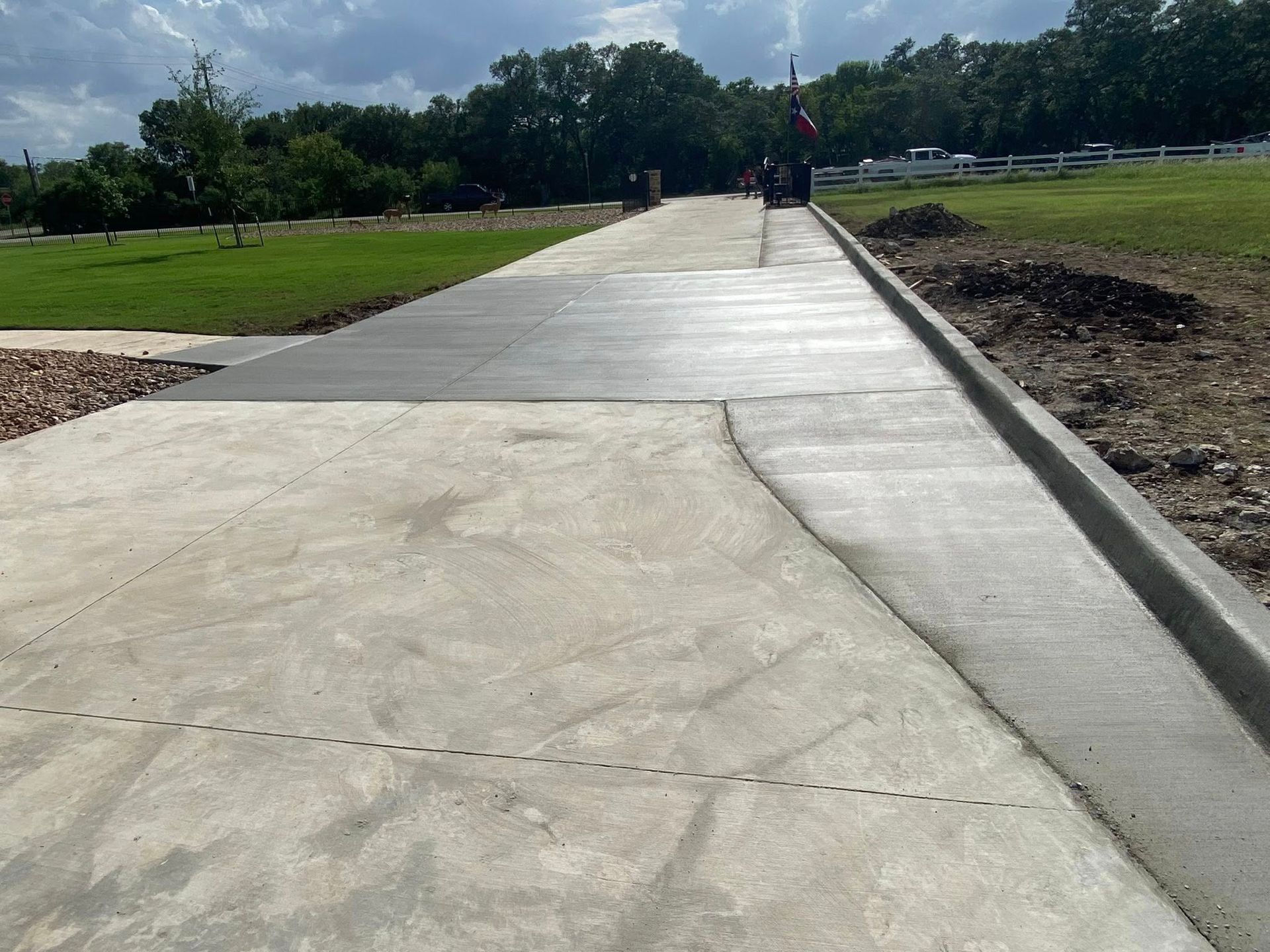 Concrete pathway with curb, leading through a grassy area toward trees