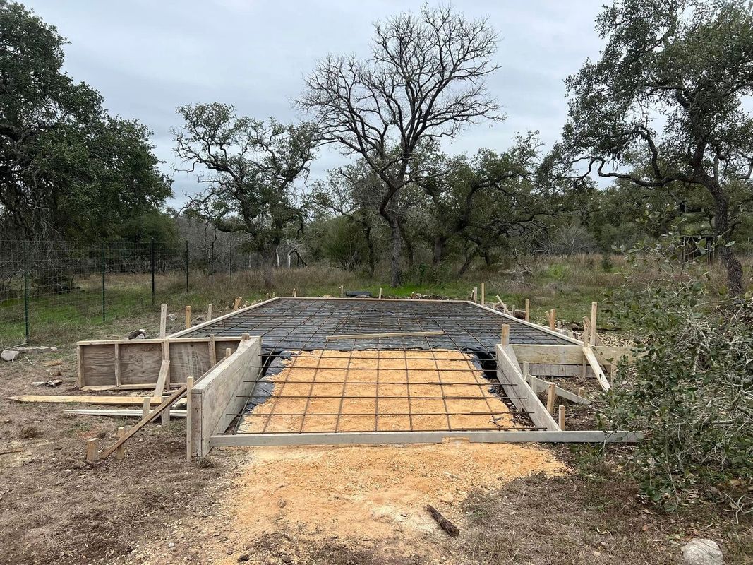 Concrete foundation with wooden forms and rebar, set outdoors in a wooded area.