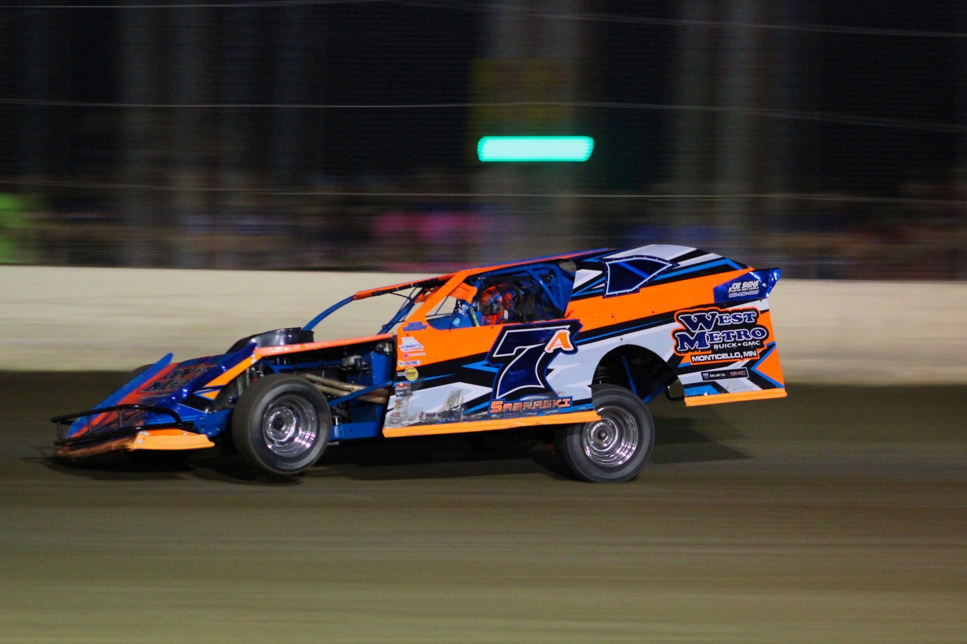 Orange and blue race car speeding on a dirt track at night. Number 7 on the side.