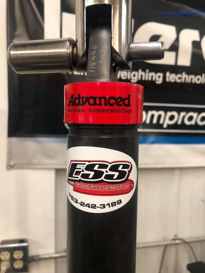 A black ESS shock absorber with a red Advanced Racing Suspension band and silver mounting hardware. Phone number 703-242-3189 is visible.