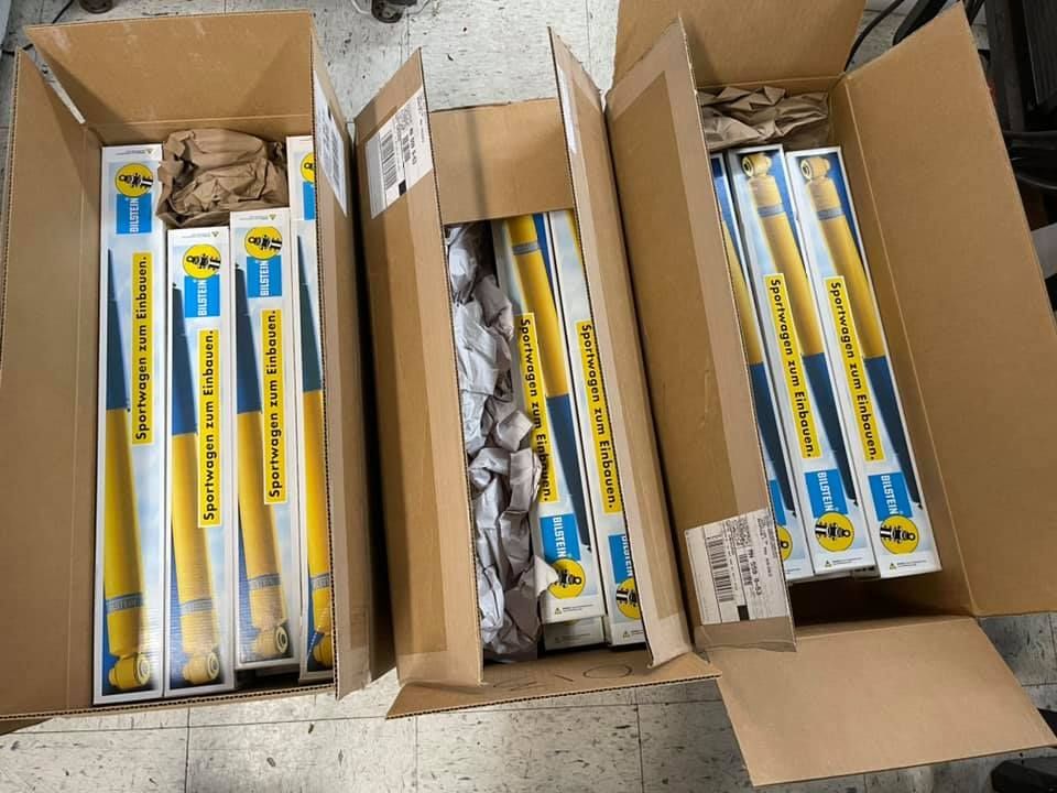 Three open cardboard boxes containing yellow and blue Bilstein shock absorbers, ready for shipping.