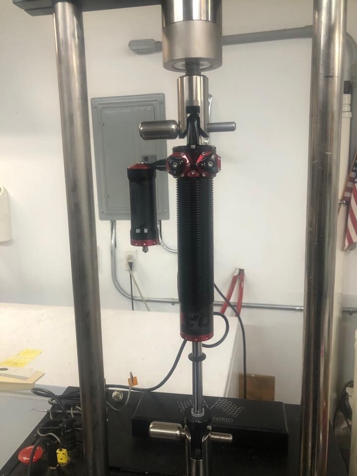 A testing machine with a black and red cylindrical component undergoing analysis; set against a white wall.