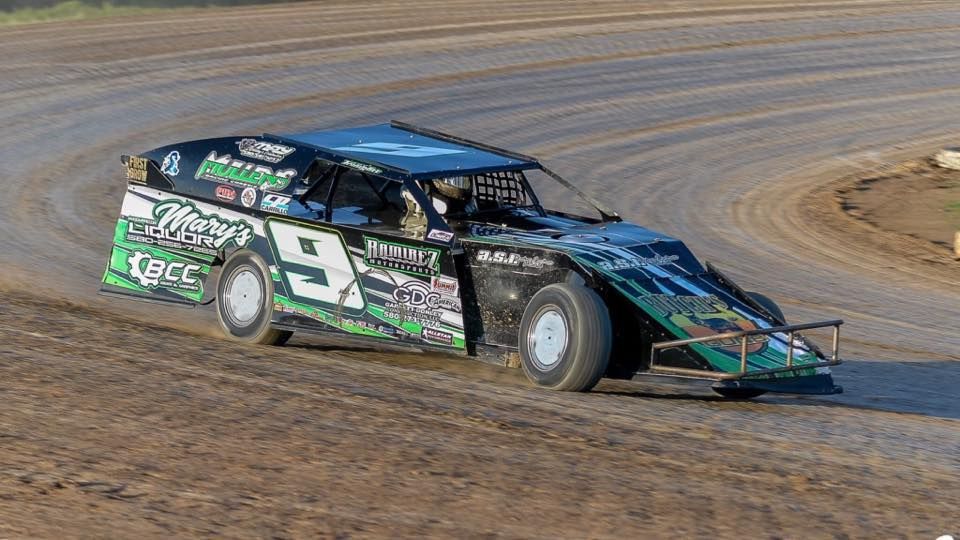 A dirt track race car, number 9, in green and black livery, cornering on a dirt track.