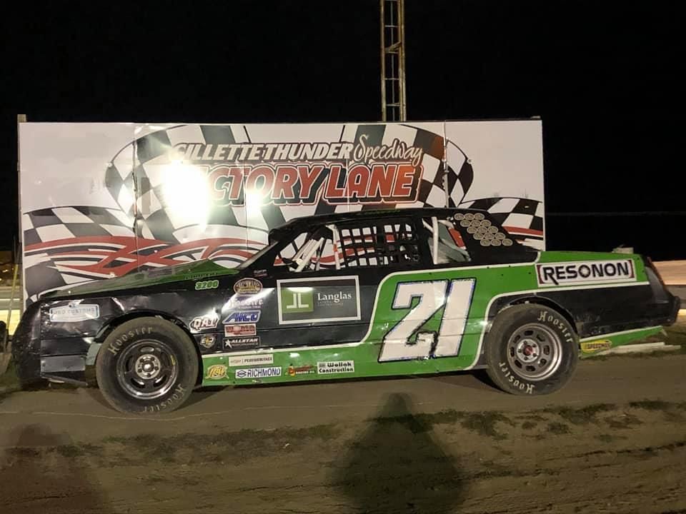 A black and green race car, number 21, on display at a racetrack with a 