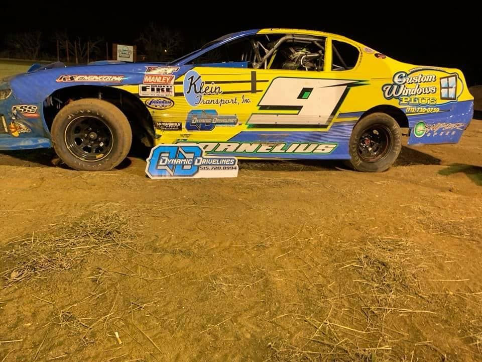 A dirt track race car, number 9, in yellow and blue livery, parked on a dirt track at night.