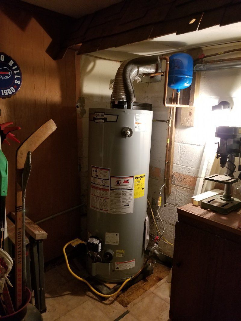 A water heater is sitting in a basement next to a clock.