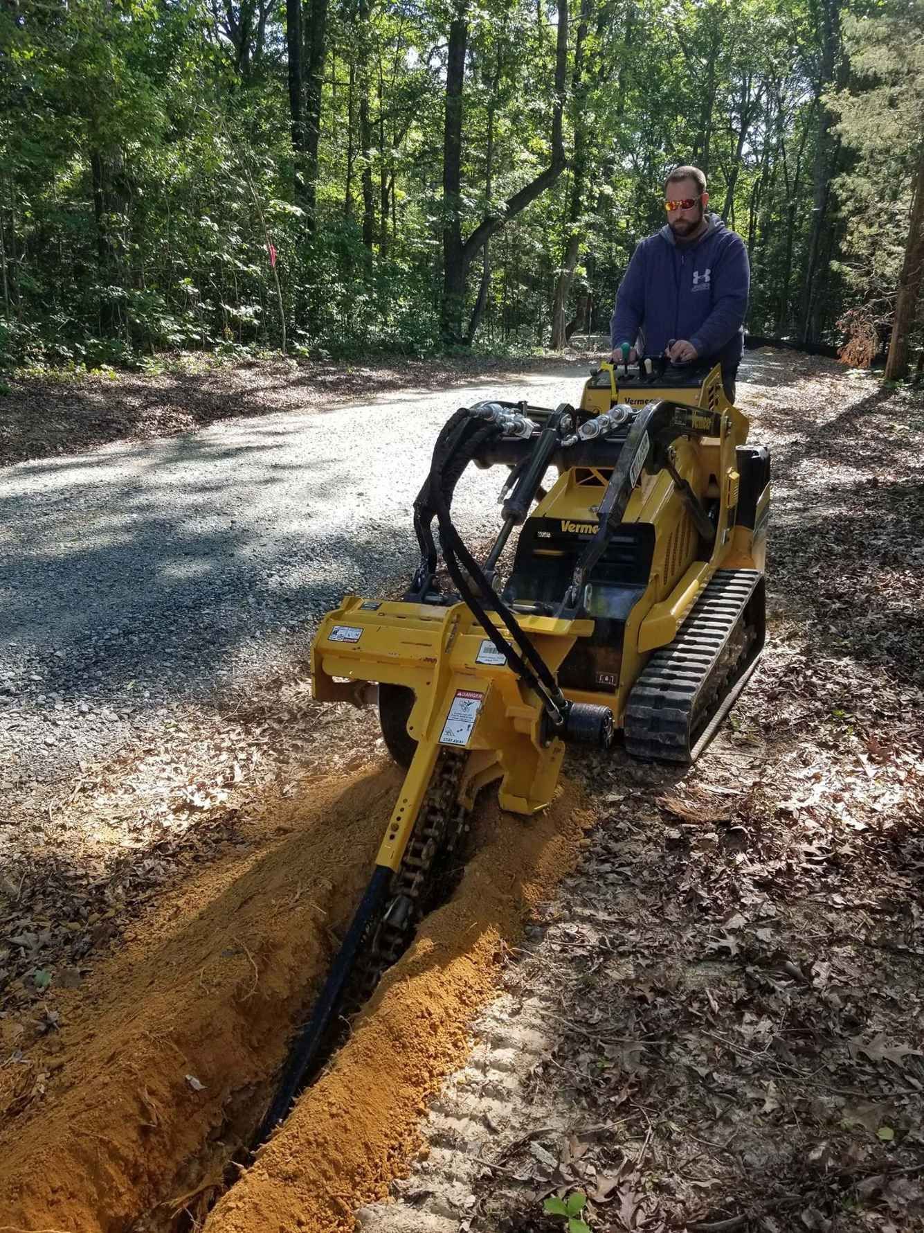 A man is driving a yellow tractor on a dirt road.