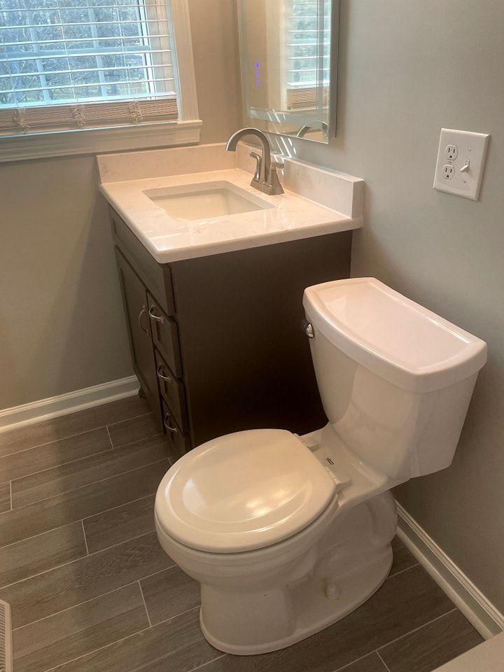 A bathroom with a toilet , sink and mirror.