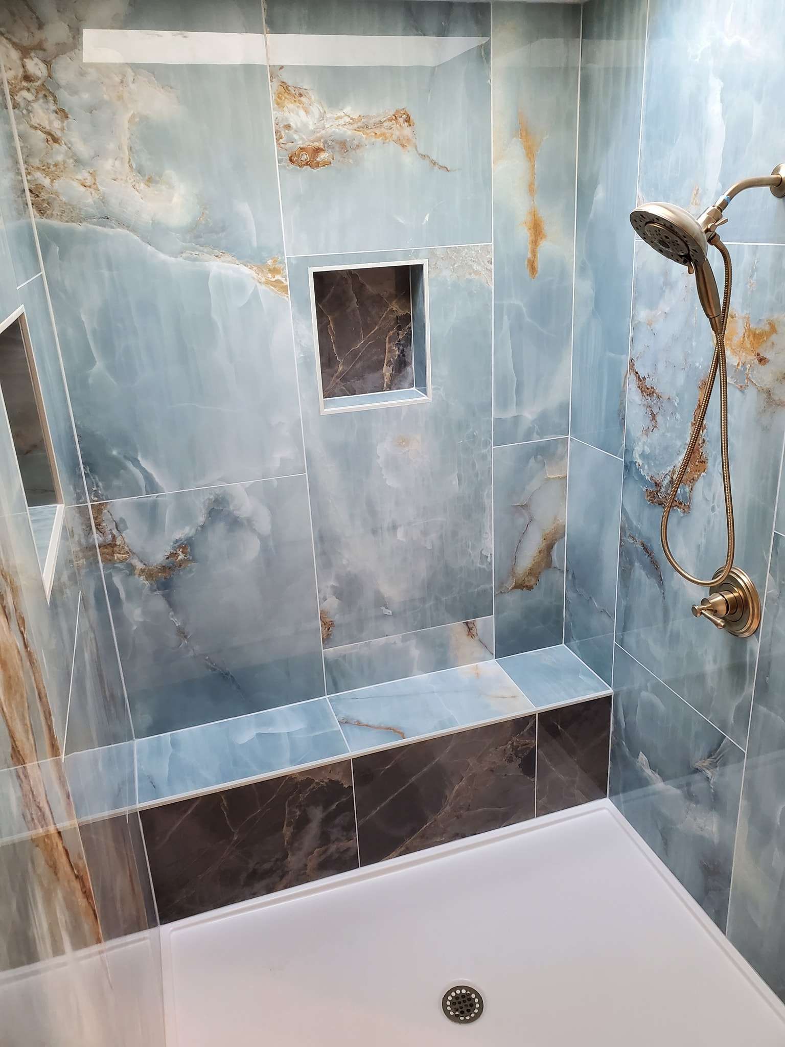 A bathroom with blue tiles and a walk in shower with a shower head.
