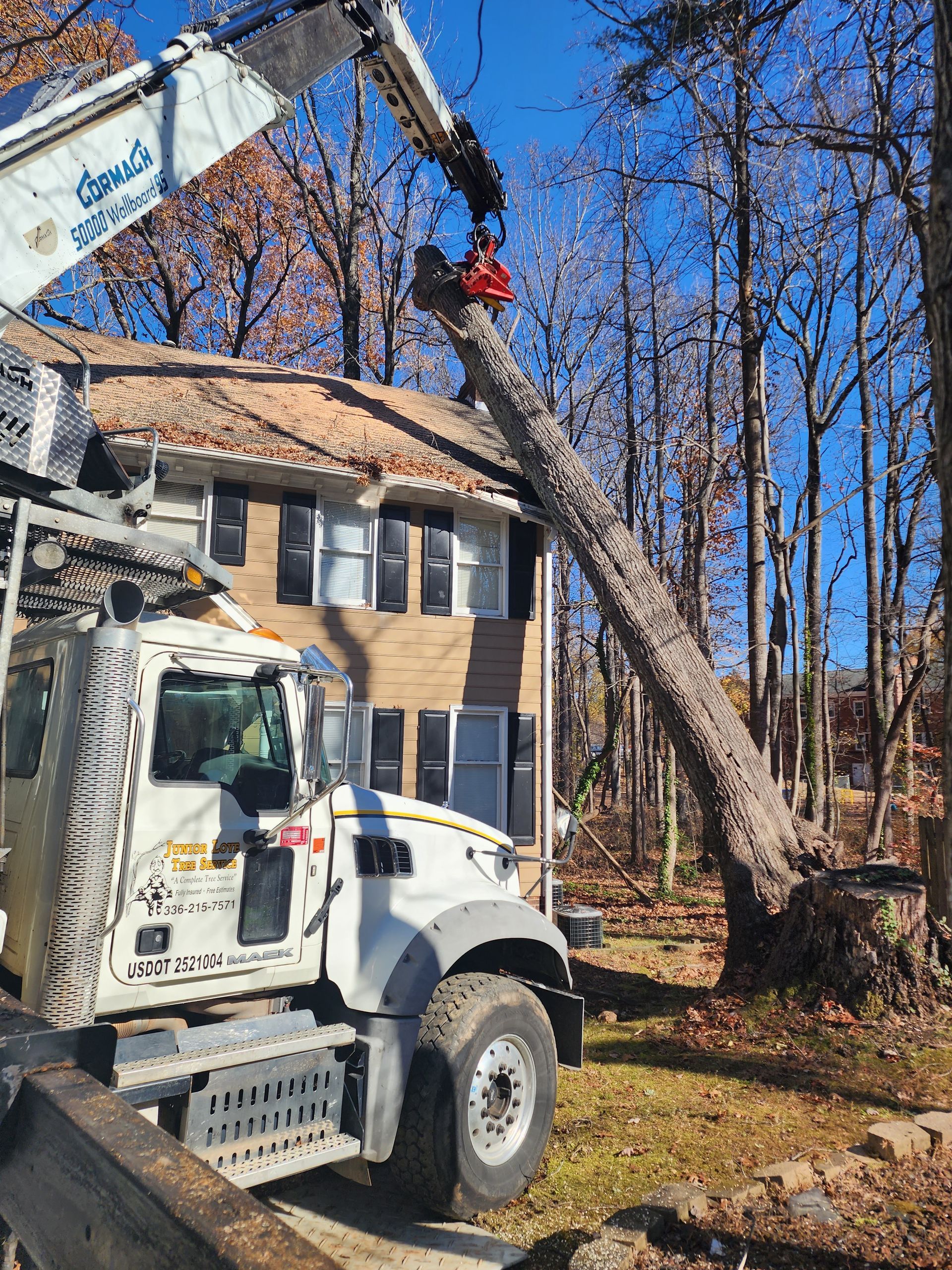 A truck is cutting a tree in front of a house.
