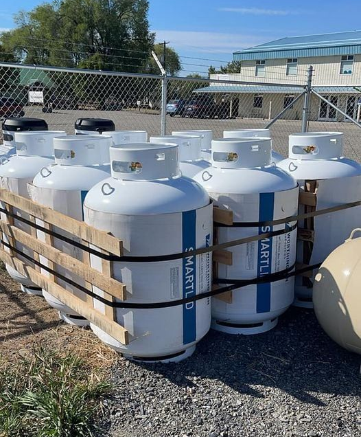Propane tanks bundled together outdoors, near a building and fence.