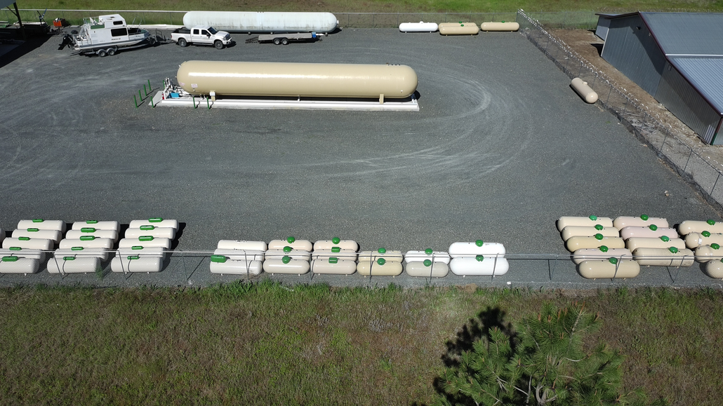 An aerial view of a gravel lot with multiple horizontal storage tanks and white containers, possibly industrial.