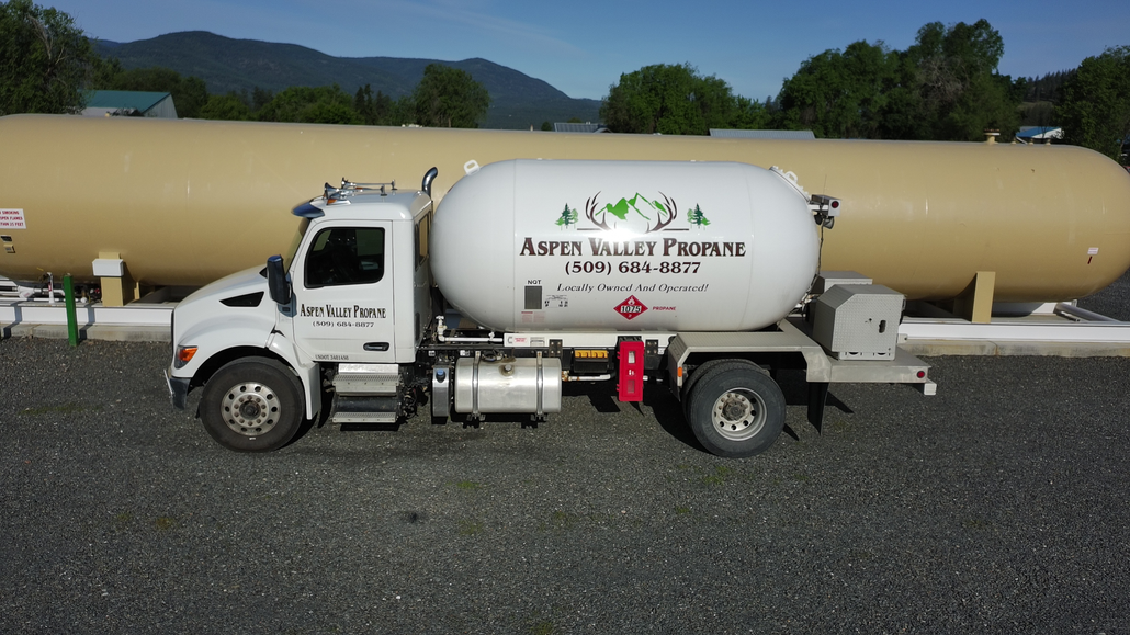 White propane truck with company logo, parked in front of large storage tanks.