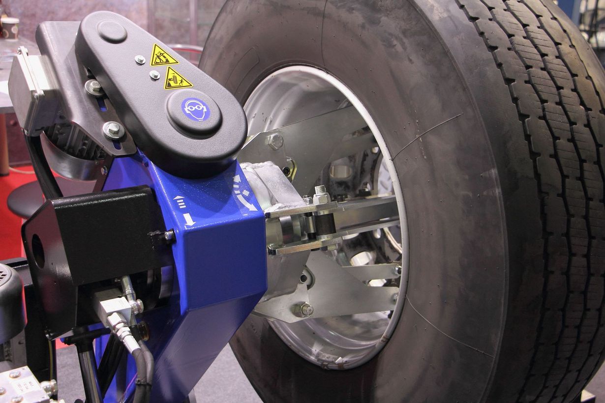 Blue wheel-alignment machine attached to a car tire in a garage, with sensors mounted on the wheel.