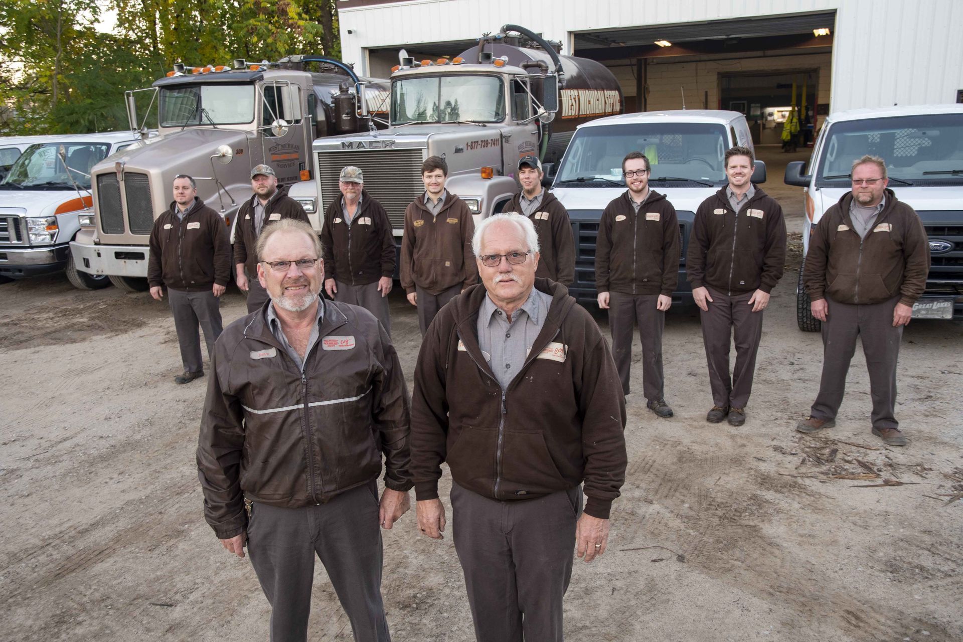 Group of men in matching jackets standing in front of trucks and garage.